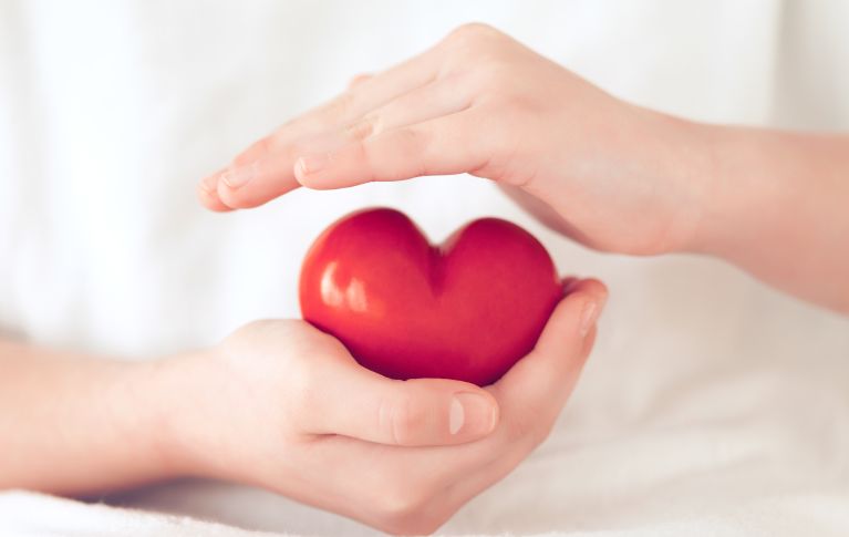 Das Bild zeigt zwei Hände, die schützend ein rotes Herz aus roter Keramik halten.