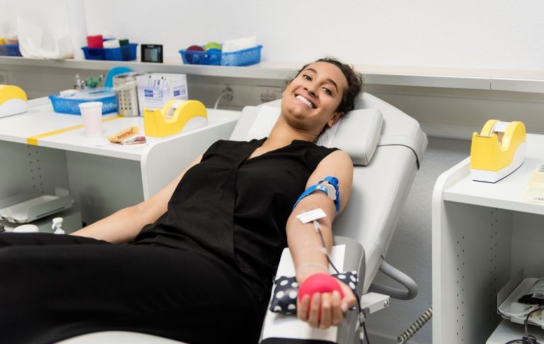 Giovane donna sdraiata sorridente su un lettino per donare il sangue.