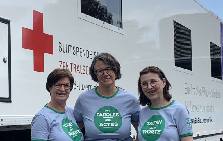 Trois femmes portant un T-shirt de la Journée de la bonne action se tiennent devant le bus de don de sang