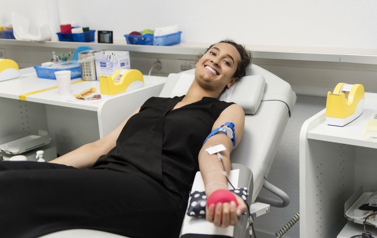 Eine junge Frau bei der Blutspende schaut lächelnd in die Kamera